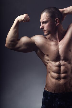 Bodybuilding. Handsome sports man posing in front of the camera on a black background. Shows his pumped-up torso and handsの写真素材
