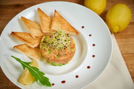 Delicious salmon tartare with avocado. Arrangement with a glass of wine and cutleryの写真素材