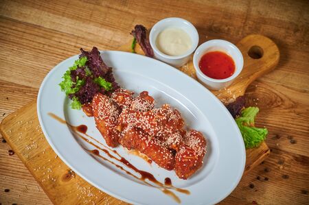 Serving of delicious spicy chicken wings with sesame seeds and sweet chili sauce on white wooden boardの写真素材