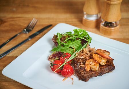 Grilling steak. Dish of meat on a plate adding with shrimp, tomatoes and salad. Arrangement with cutleryの写真素材
