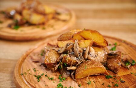 Wooden board with tasty potato wedges with mushrooms on table. Roasted potatoes with mushroomsの写真素材