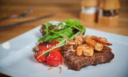 Grilling steak. Dish of meat on a plate adding with shrimp, tomatoes and salad. Arrangement with cutleryの写真素材