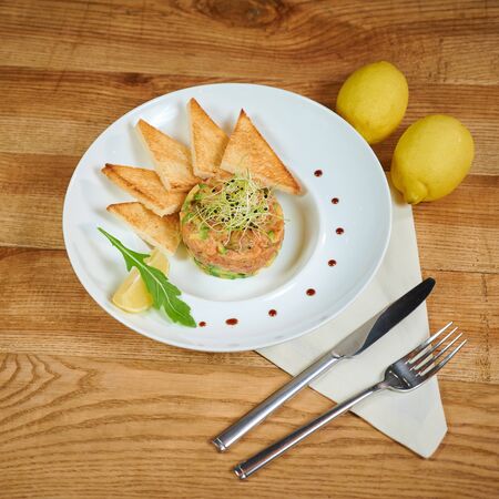 Delicious salmon tartare with avocado. Arrangement with a glass of wine and cutleryの写真素材