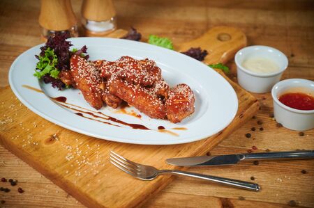 Serving of delicious spicy chicken wings with sesame seeds and sweet chili sauce on white wooden boardの写真素材