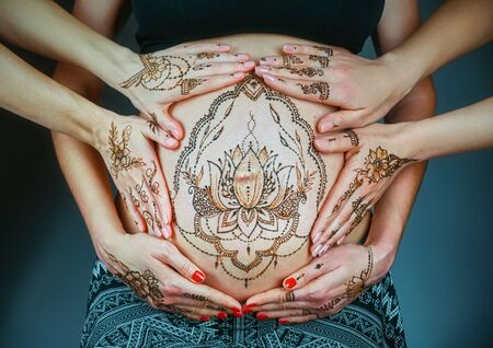 Close up of pregnant belly with mehendi henna tattoo surrounded by loving female hands. Motherhood concept, happy maternityの写真素材