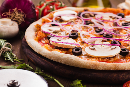 Italian pizza with mushrooms, olives and onion rings with ingredients on a dark wooden table (close)の写真素材