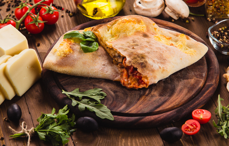 Traditional Italian Pizza "Calzone" with ingredients on a dark wooden background (close)の写真素材