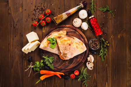 Traditional Italian Pizza "Calzone" with ingredients on a dark wooden background (close top view)の写真素材