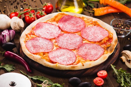 Italian pizza Pepperoni with slices of salami on the dark wooden background with ingredients around (close)の写真素材
