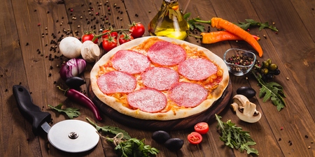Italian pizza "Pepperoni" with slices of salami on the dark wooden background with ingredients around (close)の写真素材