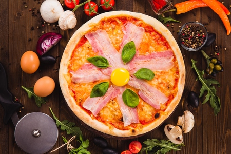Pizza Carbonara with bacon and egg yolk on the dark wooden background with ingredients around (close top view)の写真素材