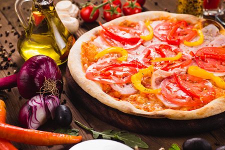 Venice pizza with ham, tomatoes and paprika on a dark wooden background with ingredients around (close)の写真素材
