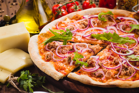 Italian pizza with chicken, onions and rucola leaves on a dark wooden background with ingredients around (close). Cut one pieceの写真素材