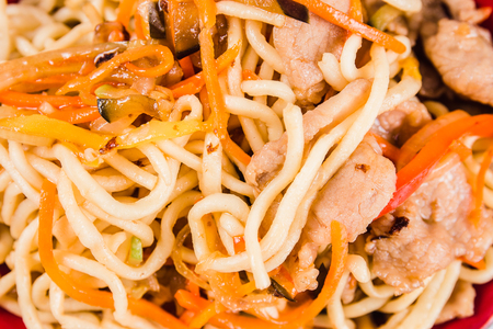 Noodles with pork, chicken and pepper on a red plate on a white background. Traditional Italian pasta. Close top viewの写真素材