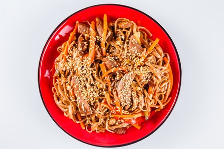 Noodles with  beef, pepper and sesame seeds on a red plate on a white background. Traditional Italian pasta. Close top viewの写真素材
