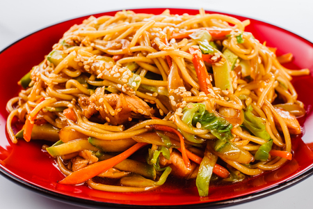Noodles with pork, pepper and sesame seeds on a red plate on a white background. Traditional Italian pasta. Closeの写真素材