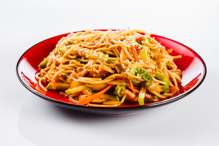 Noodles with pork, pepper and sesame seeds on a red plate on a white background. Traditional Italian pasta. Closeの写真素材
