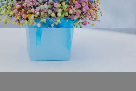 Bouquet of multi-colored gypsophila in a blue box with a bow on a gray background