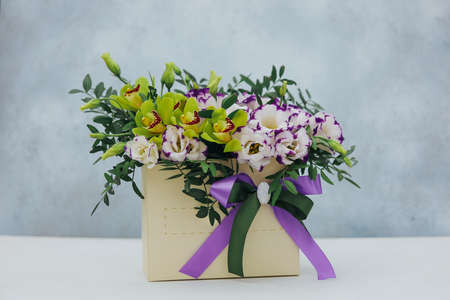 Bouquet of archidea and eustoma in a paper gift box on a gray background. In purple, white and yellow.の写真素材