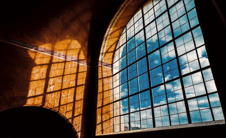 Large arched window has blue sky on background and beautiful shadows from sunlight on the yellow...