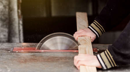 Man works on a sawmill close-up cutting a tree board. Males work. Dangerous job. Fit the board to correct size. Manufacturing in a country house.の写真素材