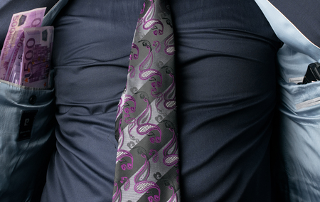 Businessman showing money and pistol in inner pocket of his suit. Concept of corrupted businessman.の写真素材