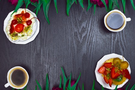 Beautiful fresh spring tulip with cup of coffee and fruit cake on dark background. Coffee time. Flower gift. Pavlova pieの写真素材