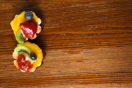 Fruit yogurt cake. Cream and yogurt based fruit filling topped with jelly. Raspberries, stawberries, oranges, kiwi on the wooden tableの写真素材