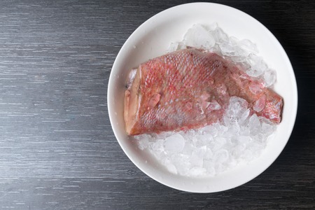 Whole raw organic fish sea perch on ice cubes in white plate on a dark table background. Top view with copy space.の写真素材
