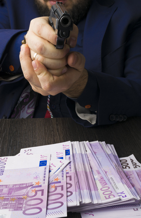 A man in blue suit with a gun directed. Cash, hundreds of euros aducted with the help of a pistol, a crime, robberyの写真素材