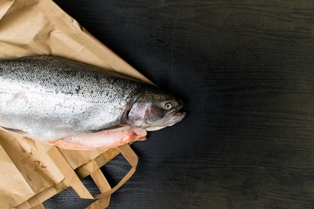 Close up shot of raw fresh rainbow trout on a black background on paper bag, Preparations for cooking delicious fishの写真素材