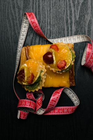 fresh homemade cakes with fruit, apricot, grape, orange, kiwi on dark wood background with tape measure. Desserts. Sweet lifeの写真素材