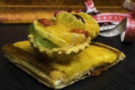 Fresh homemade cakes with fruit, apricot, grape, orange, kiwi on dark wood background with tape measure. Desserts. Sweet lifeの写真素材