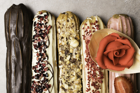 Sweet delicious colorful french eclairs decorated with marzipan red rose. Group of french dessert....