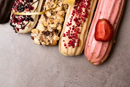 Sweet delicious colorful french eclairs. Group of french dessert with bow. Eclair background. French pastry glazed eclairs, decorated with raspberries, cream and chocolate. Variety Selectionの写真素材