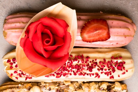 Sweet delicious colorful french eclairs decorated with marzipan red rose. Group of french dessert. Eclair background. French pastry glazed eclairs, decorated with raspberries, cream and chocolate. Variety Selectionの写真素材