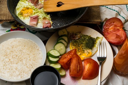 Traditional breakfast with bacon, fried eggs, tomatoes, cucumber, dill and dairy porridge in bowl. Health morning foodの写真素材