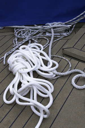 Close-up of a mooring rope with a knotted end tied around a cleat on a wooden pier/ Nautical mooring...