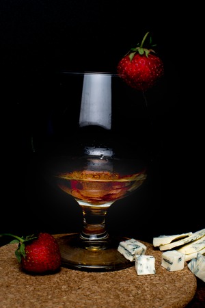 Still life with Cognac and french blue cheese on a wooden board. Glass with cognac, cheese, strawberry on a wooden backgroundの写真素材