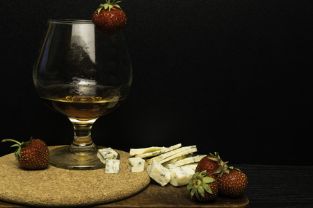 Still life with Cognac and french blue cheese on a wooden board. Glass with cognac, cheese, strawberry on a wooden backgroundの写真素材