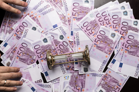Big amount of Five hundred notes of European Union Currency, hourglass and men hands. Time and moneyの写真素材