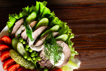 boiled tongue slices with vegetables tomatoes red pepper cucumber lettuce peas with mayonnaise on the wooden tableの写真素材