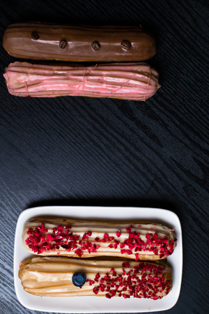 delicious colored eclairs with coffee beans, blueberry, raspberry on black wooden table
