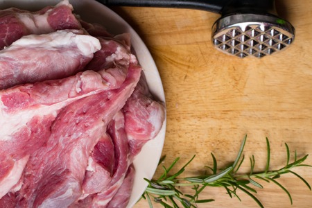 Pieces of raw pork steak with rosemary and butcher hummer, on dark wooden background in rustic styleの写真素材
