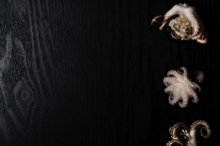 Raw octopus in oil isolated on black table, ready to eat. Seafood. Top view with space for your recipeの写真素材