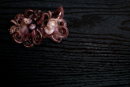 Raw octopus in oil isolated on black table, ready to eat. Seafood. Top view with space for your...