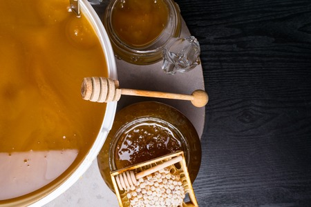 honeycomb and fresh honey in white bucket and in glass jar, wooden sticks