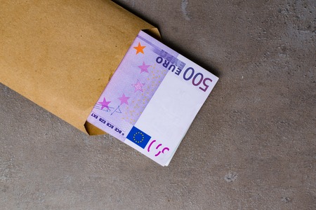 Five hundert euro bank notes in beige envelope, isolated on a grey background