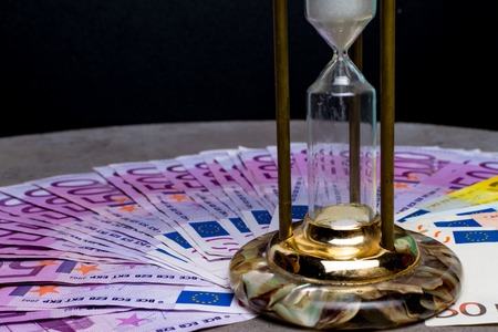 many 500 euro banknotes background with hourglass. EU currency, save money and time concept