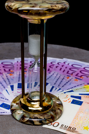 many 500 euro banknotes background with hourglass. EU currency, save money and time concept